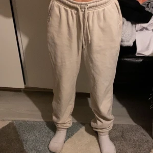 Beige mjukisbyxor med dragsko - Säljer ett par beige mjukisbyxor med resår i midjan och dragsko. Byxorna har en avslappnad passform och är perfekta för chill dagar hemma. Mjukt material och muddar vid bensluten för extra komfort.