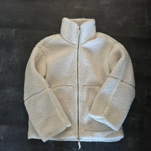 Beige teddyjacka från H&M - Mysig beige teddyjacka från H&M med hög krage och dragkedja framtill. Jackan har två fickor och är helfodrad för extra komfort. Perfekt för kyliga dagar när du vill vara både varm och snygg. Perfekt nu inför lite kyligare dagar❣️ i väldigt bra skick!🥰hör av er vid frågor