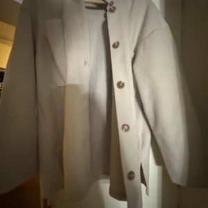 Beige overshirt med knappar - Säljer en beige overshirt med stora bröstfickor och knäppning framtill. Jackan har lång ärm och en rak, lite boxig passform. Perfekt att slänga över en hoodie eller t-shirt för en chill look.