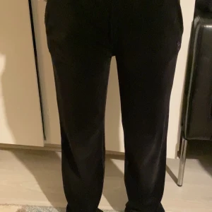 Svarta mjukisbyxor från Juicy Couture - Svarta mjukisbyxor från Juicy Couture med strassdetaljer och texten 'Juicy' på baksidan. Byxorna har normal passform och är tillverkade i ett mjukt material som känns skönt mot huden.