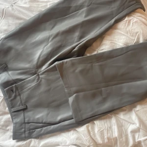 Gråa skinnbyxor från Desin By Si - Säljer ett par gråa skinnbyxor från Desina by Si med normal passform och raka ben. Byxorna har klassisk midja, knapp och dragkedja framtill samt diskreta fickor. Perfekta för dig som vill ha en stilren look med edge.