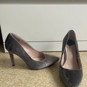 Grå sammetspumps med klack - Säljer ett par eleganta grå pumps i sammet med smal klack och rund tå. Perfekta för dig som vill ha en stilren och klassisk sko med lite extra lyxig känsla. Passar till många olika outfits!