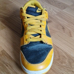 Nike Dunk Low svart och gul - Säljer ett par Nike Dunk Low i svart och gul färg. Skorna har klassisk Nike-logga på sidan och häl, gul snörning och vit sula. Perfekta för dig som vill sticka ut med en färgstark sneaker.