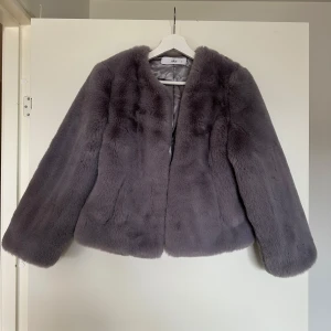 Grå pälsjacka - Säljer en fluffig och mjuk grå pälsjacka med lång ärm och rund halsringning. Jackan har en klassisk och stilren look utan synliga detaljer framtill. Perfekt för dig som vill ha en trendig och varm jacka.
