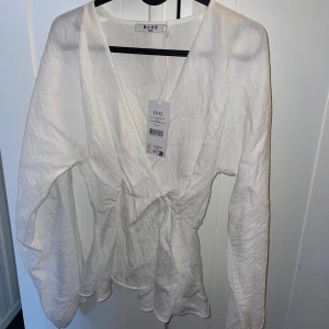 Vit v-ringad blus från NA-KD - Säljer en vit blus från NA-KD i storlek 32. Blusen har v-ringning, långa ärmar och markerad midja. Tillverkad i ett lätt och luftigt material som ger en avslappnad men stilren look.