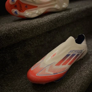 Adidas F50+ fotbollsskor ELITE - Snygga Adidas F50 fotbollsskor i vitt, rött och blått. Perfekta för snabba spelare som vill ha lättviktiga skor med bra passform.