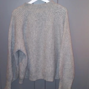 Grå stickad tröja - Mysig grå stickad tröja med ribbad struktur och lång ärm. Perfekt för kyligare dagar och enkel att matcha med olika outfits. Klassisk modell med rund halsringning.