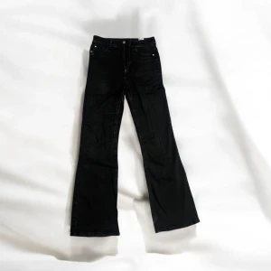 Svarta bootcut jeansbyxor från Cubus Jane Boot - Svarta jeansbyxor från Cubus Jane Boot med bootcut-modell och hög midja. Klassisk femficksdesign och stängning med dragkedja och knapp. Perfekta för dig som gillar en tidlös och stilren look.