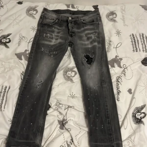 Grå slitna jeans från Dsquared2 - Säljer ett par grå jeans från Dsquared2 med slitningar och hål på låret. Jeansen har fem fickor, knappgylf och en tvättad look med ljusare partier. Märkeslapp bak i midjan och Dsquared2-etikett vid fickan.