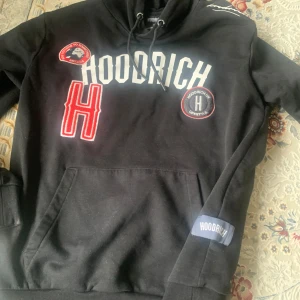 Svart hoodie från Hoodrich med patchar - Säljer en svart hoodie från Hoodrich med stora vita bokstäver och flera patchar på bröstet. Använd några gånger, köpt för 1100 kr