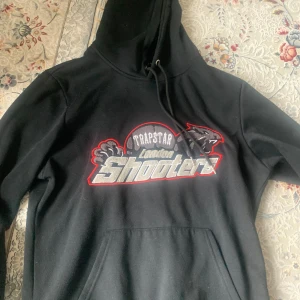 Svart hoodie från Trapstar London Shooters - Säljer en svart hoodie från Trapstar med tryck 'London Shooters' på bröstet i grått, vitt och rött. Köpt i england, nytt skick 