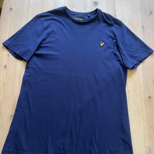 Mörkblå t-shirt från Lyle & Scott - Säljer en stilren mörkblå t-shirt från Lyle & Scott med klassisk passform. T-shirten har korta ärmar och pryds av den ikoniska gula loggan broderad på bröstet. Perfekt till jeans eller shorts. Size L 44/68