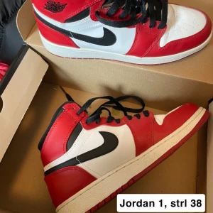Nike Air Jordan 1 Chicago - Klassiska Nike Air Jordan 1 i Chicago-färg. Skorna har röd, vit och svart färgkombination med svart swoosh och snörning. Hög modell med rund tå och platt sula. Perfekta för dig som gillar streetwear och sneakers.