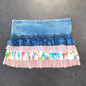 Minikjol med volang och jeansmidja - En minikjol med jeans upptill och flera lager volanger i rosa tyll och färgglatt mönstrat tyg. Kjolen har dragkedja i sidan och låg midja. Strl: M, lite stretchig.  Mått: Midja 76 cm.  /  Spara skärmtid, besök våra butiker i Sthlm, Malmö & Gbg. New arrivals daily + studentrabatt i alla våra butiker! Hitta till din närmsta butik på humansecondhand.se.   HUMANA Second Hand erbjuder 14 dagars retur, även via plick. Returer skickas med PostNord. Vid retur kontakta support@plick.se.