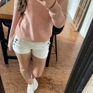 Vita shorts med knappar - Säljer ett par vita shorts med dekorativa silverfärgade knappar på sidorna. Shortsen har normal passform och är tillverkade i ett bomullsliknande material. Perfekta för sommaren och har en klassisk look med fickor både fram och bak.