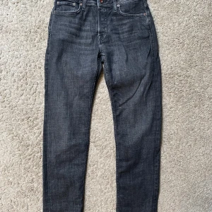 Mörkgrå jeans från Jack & Jones - Snygga mörkgrå jeans från Jack & Jones, modell Mike Tapered. Klassisk femficksdesign, regular rise och tapered fit som smalnar av nedtill. Perfekta för en stilren och avslappnad look. Helt oanvänd, prislapp kvar