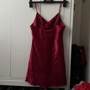 Röd satin klänning med tunna axelband - Säljer en röd satin klänning med tunna justerbara axelband och subtilt blommönster. Klänningen har en lätt glansig yta och figurnära passform med v-ringad byst. Perfekt för fest tillfällen eller som pyjamas!♥️ Storleken är M men passar också mig som har S.