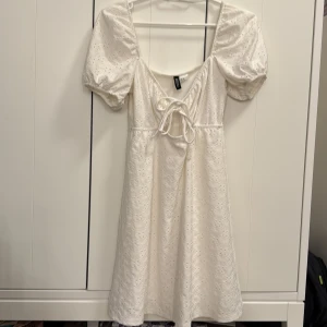 Vit klänning med puffärmar och knytning - Söt vit klänning med broderade detaljer, puffärmar och knytning framtill. Klänningen har en fyrkantig ringning och är tillverkad i ett lätt bomullstyg. Perfekt för sommarens alla tillfällen eller skolavslutning. Storlek xs men passar nog även S!  