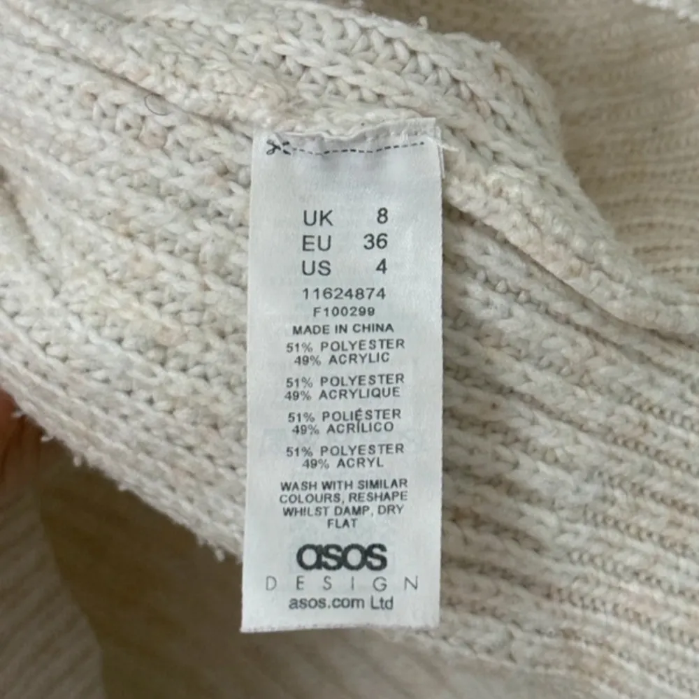 Säljer en beige stickad tröja från ASOS DESIGN med bred v-ringning och lång ärm. Tröjan har en avslappnad passform och är gjord i en mjuk blandning av polyester och akryl. . Neuletakit & Villapaidat.