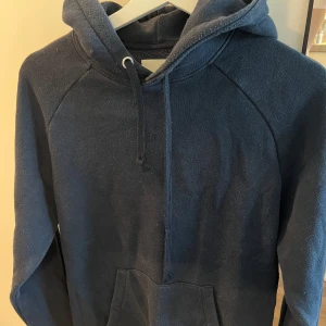 Mörkblå hoodie A Day March - Säljer en enkel och stilren mörkblå hoodie med huva och dragsko. Tröjan har en stor magficka och långa ärmar, perfekt för en avslappnad look. Passar både till skolan och häng med kompisar.