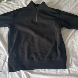 Svart fleece-tröja med dragkedja från H&M - Svart fleece-tröja från H&M med halv dragkedja framtill och hög krage. Modellen är relaxed fit och materialet är mjukt och varmt, perfekt för kyligare dagar. Enkel och stilren design utan synliga mönster eller detaljer.