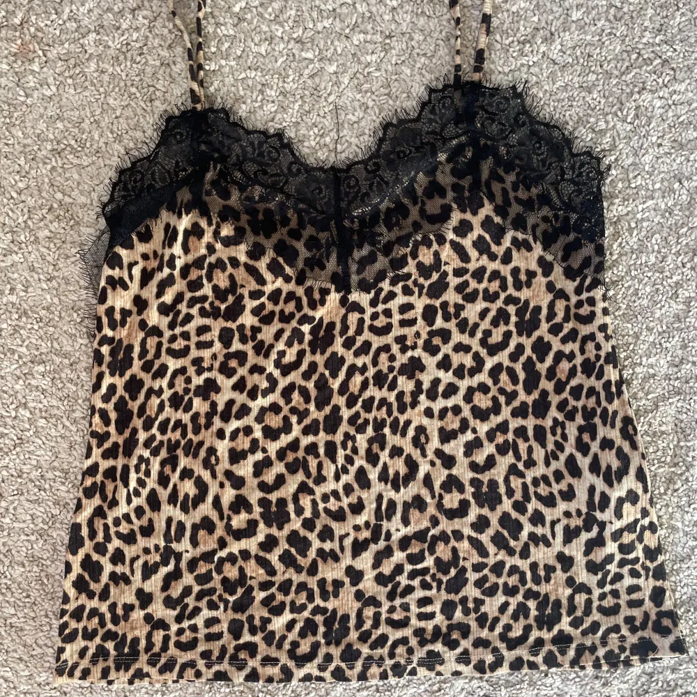 Säljer ett leopardmönstrat linne med tunna axelband och svart spets upptill. Toppen har en croppad passform och är perfekt för dig som vill sticka ut med ett djurmönster. Materialet känns mjukt och följsamt.. Yläosat.