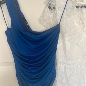 Blå one shoulder topp från BikBok - Säljer en snygg blå one shoulder topp från BikBok. Toppen har draperad design och smala axelband. 