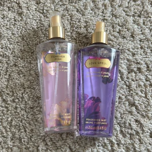 Victoria's Secret Body Mists - Två body mists från Victoria's Secret: Forever Pink i ljusrosa flaska och Love Spell i lila flaska. Båda har guldiga spraymunstycken och detaljer. Doftnoter av blomma och persika. Den lila är typ mer än halvfull, den rosa är ungefär en 1/4 kvar i.