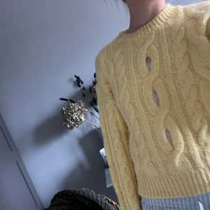 Gul stickad tröja med flätmönster - Säljer en söt gul stickad tröja med grovt flätmönster och rund hals. Tröjan har långa ärmar och ribbade muddar vid ärmslut och nederkant. Perfekt för lager-på-lager och ger en mysig känsla.