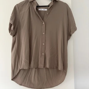 Brun kortärmad skjorta från Samsøe Samsøe - Säljer en brun kortärmad skjorta från Samsøe Samsøe i modellen Maja. Skjortan har knappar framtill, klassisk krage och en avslappnad passform med något längre bakstycke. Perfekt till sommarens alla tillfällen.