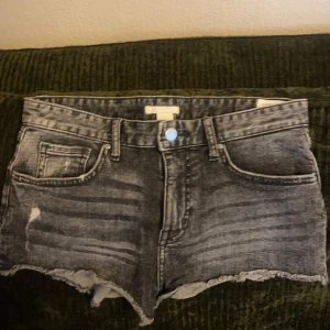 Grå jeansshorts med fransig kant - Säljer ett par grå jeansshorts från H&M med fransig kant och slitningar framtill. . Perfekta för sommaren och ger en cool, avslappnad look.