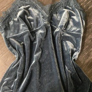 Blå nattlinne med spetsdetaljer - Supersnygg blå nattlinne med vacker spets upptill och nertill. Klänningen/linnet  har en mjuk, glansig yta och feminina spetsdetaljer som ger en lyxig känsla. Perfekt för dig som vill sticka ut med en elegant look.