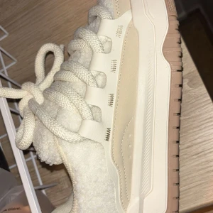 Beige sneakers med teddyfoder och grova snören - Säljer ett par beige sneakers med teddyfoder och extra grova snören. Skorna har en chunky sula i beige och brunt, samt detaljer i syntetmaterial. Perfekta för dig som vill ha en unik och trendig look.