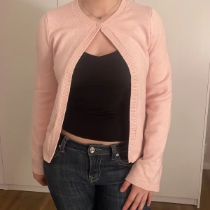 Ljusrosa kofta från Gina Tricot - Säljer en söt ljusrosa kofta från Gina Tricot i storlek S. Koftan är öppen framtill med en liten knäppning vid halsen och har långa ärmar. Perfekt att slänga över en topp för en enkel och snygg look.