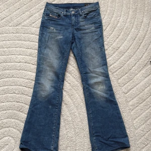 Blå bootcut jeans från Diesel - Säljer ett par blå bootcut jeans från Diesel, modell LOWLEEH-J JJJ-N. Jeansen har klassisk femficksdesign, låg midja och slitna detaljer framtill för en cool look. Byxorna är i storlek 12 Y. (UPPSYDDA hos skreddare!). Längden på jeansen är nu 90cm. Säljer dessa för 400 kr! Jeansen är nästan helt oanvända, har använt dom en eller två gånger.