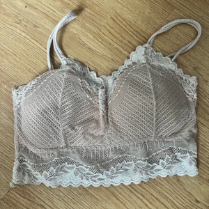 Beige spets bralette från Dana - Säljer en beige bralette från Dana med vacker spets och tunna axelband. Toppen har fina spetsdetaljer både upptill och nedtill samt lätt vadderade kupor. Perfekt för lager-på-lager eller som en snygg detalj under en skjorta.