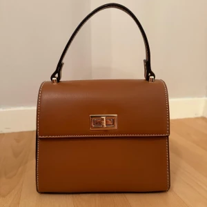 Brun handväska från Gina tricot  - Varm fin brun färg med ett guldspänne. Finns ett kort handtag med följer även med ett längre band. 