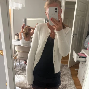 Vit kofta med pärlknappar - Superfin vit kofta från Zara med rund hals och långa ärmar. Koftan har dekorativa pärlknappar som ger en lyxig känsla och är stickad i ett mjukt material. Perfekt att slänga över en topp för en söt och stilren look.