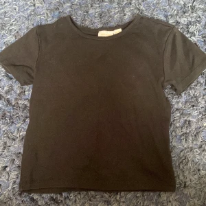 Svart croppad topp från Gina Tricot - En basic svart croppad topp från Gina Tricot med rund halsringning och korta ärmar. Enkel och stilren modell i mjuk bomull som passar perfekt till jeans eller kjol. Snygg att styla lager på lager eller bara som den är.