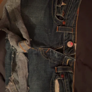 True Religion jeansshorts, mörkblå, stl 28 - Snygga mörkblå jeansshorts från True Religion med råa kanter och ikoniska kontrastsömmar. Klassiska fickor med tryckknappar och detaljerad bakficka. Perfekt för dig som gillar streetstyle och vill sticka ut med ett par statement shorts. Aldrig använda.