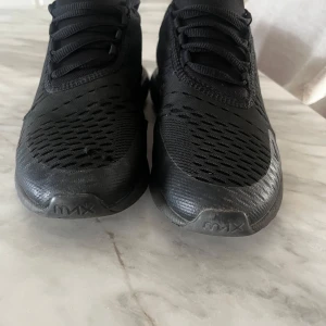 Svarta Nike Air Max 270 sneakers - Svarta Nike Air Max 270 sneakers med mesh-ovandel och tydlig Air Max-dämpning i hälen. Snygg sportig look med diskreta loggor och snörning. Ovandelen är i syntet och mesh för bra andningsförmåga. Perfekta för dig som gillar streetstyle och sportig vibe.