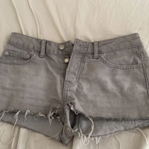 Grå jeansshorts från 157, XS - Gråa jeansshorts från 157 i storlek XS. De är lågmidjade , fransiga kanter och klassisk femficksdesign. Perfekta för en chill sommarlook med avslappnad vibe. Bälteshällor och dubbla knappar framtill ger extra detaljer.