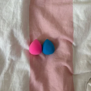 Två beautyblenders i rosa och blå - Säljer två smidiga beautyblenders i droppform, en i stark rosa och en i klarblå färg. Perfekta för att applicera foundation eller concealer och få en jämn finish. Mjukt material som gör det enkelt att blenda ut sminket för ett flawless resultat. Två mindre modeller av en vanlig Beautyblender
