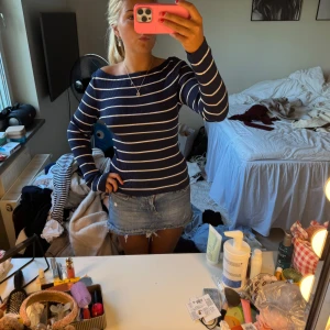 Marinblå randig ribbad tröja - Säljer en marinblå långärmad tröja med vita horisontella ränder. Tröjan är ribbad och har en offshoulder-design som ger en snygg och avslappnad look. Perfekt till jeans eller kjol för en fräsch stil.