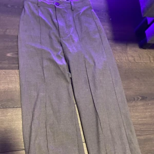 Grå kostymbyxor - Snygga grå kostymbyxor med klassiska pressveck och hög midja. Byxorna har raka ben och stängs med knapp och dragkedja. Perfekta för en clean och stilren look.