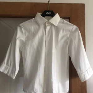 Vit skjorta med trekvartsärm - Klassisk vit skjorta i bomull med trekvartsärm och stilren krage. Skjortan har knappar framtill och en enkel, clean look som passar till många olika outfits. Perfekt för dig som gillar en tidlös och fräsch stil.💕☀️