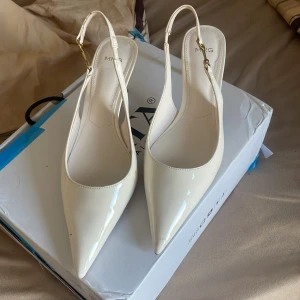 Vita pumps med spetsig tå från MNG - Intressekoll Snygga vita pumps från MNG med spetsig tå och smal klack. Skorna har en elegant slingback-rem med guldfärgade spännen och är tillverkade i glansigt syntetmaterial. Perfekta för dig som vill ha en clean och chic look. Använd en gång, har en liten fläck på vänstra foten. Köpa för 720kr från Asos 