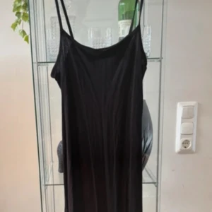 Svart långklänning från Gina Tricot - Enkel och stilren svart långklänning från Gina Tricot med smala axelband och rak passform. Klänningen har en slits 