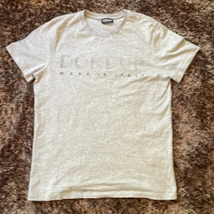 Ljusgrå t-shirt från Dondup - Säljer en stilren ljusgrå t-shirt från Dondup med diskret tryck framtill där det står Dondup made in italy. T-shirten har klassisk passform, rund halsringning och är tillverkad i mjuk bomull. Har bara använt ett fåtal gånger så den är i mycket bra skick. Skriv om ni har några funderingar.