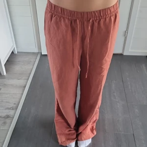 Rostfärgade linnebyxor med snörning S - Säljer ett par rostfärgade linnebyxor i avslappnad passform. Byxorna har resår och snörning i midjan samt fickor i sidorna. Perfekta för chill dagar och riktigt sköna tack vare linnemixen. Styla med en enkel t-shirt eller hoodie för en laidback vibe.